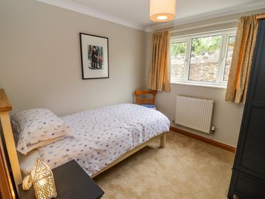 A bedroom with a single bed pillow bedside table wooden chair curtains and a wardrobe at Corner House in Cinderford