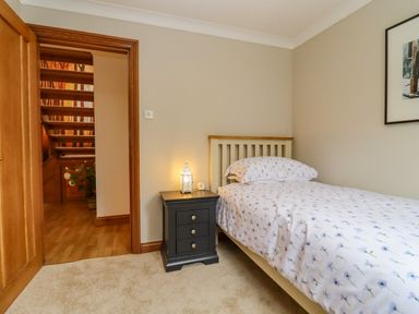 A bedroom with single bed and nightstand next to an open door showing a staircase at Corner House in Cinderford