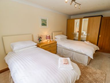 A bedroom with two single beds a wooden wardrobe and a nightstand with a lamp and flowers at Corner House in Cinderford