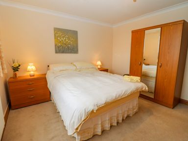A bedroom with a double bed two bedside tables two lamps a wooden wardrobe and a painting on the wall at Corner House in Cinderford
