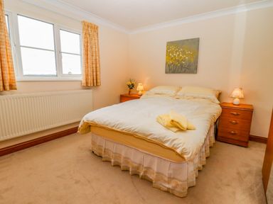 A bedroom with a double bed flanked by two wooden nightstands with lamps and a window with curtains at Corner House in Cinderford