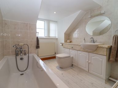 A bathroom with a bathtub toilet sink mirror and cabinets at Corner House in Cinderford