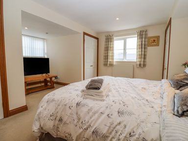 A bedroom with a bed with folded towels and a television on a wooden stand by the window at Corner House in Cinderford