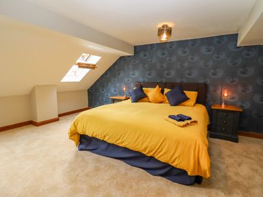 A bedroom with a slanted ceiling window a bed with yellow and blue bedding and two nightstands at Corner House in Cinderford