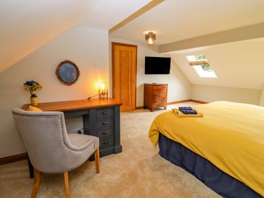 A bedroom with a desk and chair a dresser a wall-mounted tv and a bed with a yellow duvet at Corner House in Cinderford