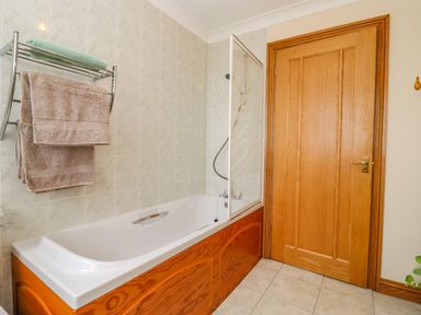 A bathroom with a bathtub with wooden paneling towels on a rack and a wooden door at Corner House in Cinderford