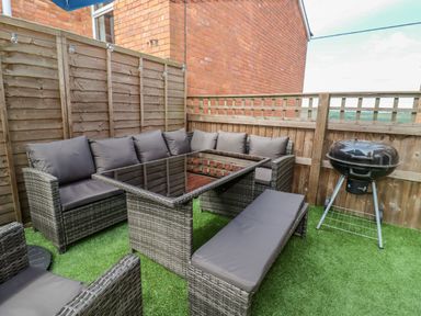 An outdoor patio with wicker seating furniture a glass top table and a charcoal barbecue grill at Corner House in Cinderford