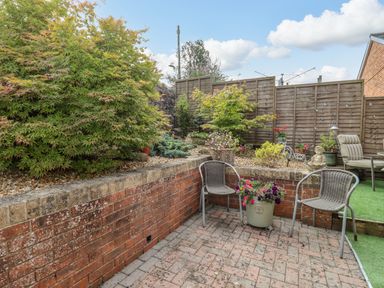 An outdoor patio area with two chairs a flower pot and garden plants behind a brick wall at Corner House in Cinderford