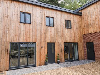 A modern wooden house exterior with three upper windows three sets of black framed doors and two potted plants at Stag Cottage in Lytchett Matravers