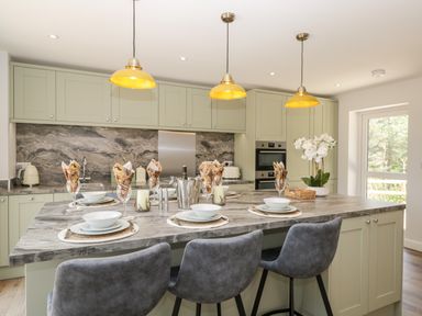 A kitchen with an island set for dining under three yellow pendant lights at Stag Cottage in Lytchett Matravers