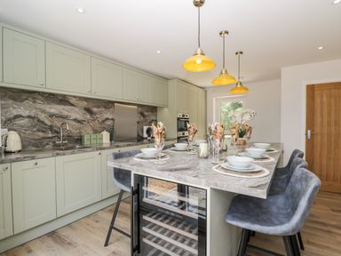 A kitchen with a marble countertop island set with dishes and grey chairs at Stag Cottage in Lytchett Matravers