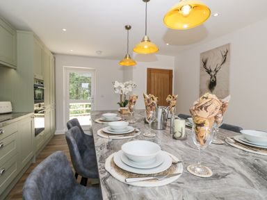 A kitchen with a marble countertop island set with plates bowls and glasses with printed napkins and pendant lights at Stag Cottage in Lytchett Matravers
