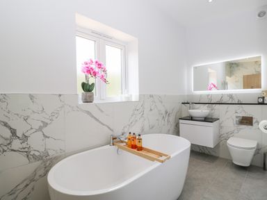 A bathroom with a freestanding bathtub and a pink flower on the windowsill at Stag Cottage in Lytchett Matravers