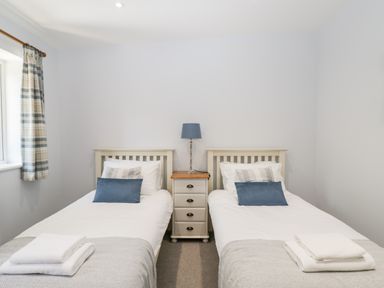 A bedroom with two single beds a nightstand with a lamp between them and a window with plaid curtains at Stag Cottage in Lytchett Matravers