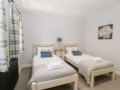 A bedroom with two single beds a nightstand with a lamp and a flower painting on the wall at Stag Cottage in Lytchett Matravers