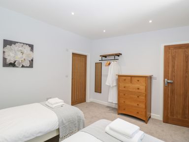 A bedroom with two single beds with folded towels a wooden chest of drawers two wooden doors and a wall-mounted coat rack with robes at Stag Cottage in Lytchett Matravers