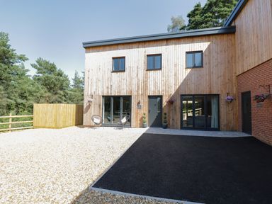 A modern wood clad house with black framed windows and doors with gravel and asphalt driveway at Stag Cottage in Lytchett Matravers