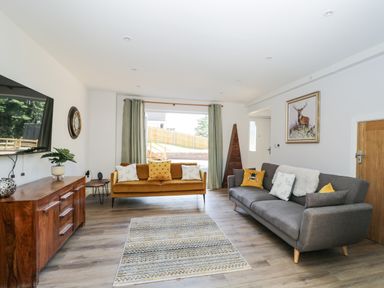 A living room with two sofas a wooden cabinet a wall clock and a painting at Stag Cottage in Lytchett Matravers
