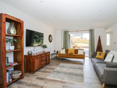 A living room with two sofas a wooden bookshelf a wooden sideboard a wall-mounted television and a rug at Stag Cottage in Lytchett Matravers