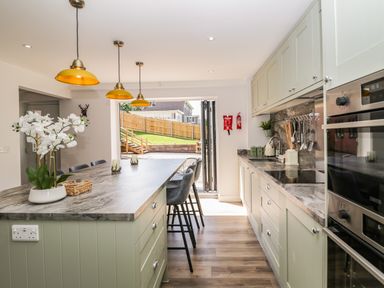 A kitchen with a marble countertop island stools and hanging lights with an open door to a garden at Stag Cottage in Lytchett Matravers