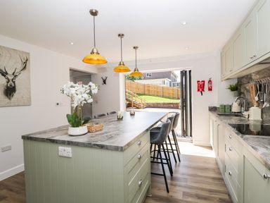 A kitchen with a marble countertop island and bar stools pendant lights and an open door leading to a garden at Stag Cottage in Lytchett Matravers
