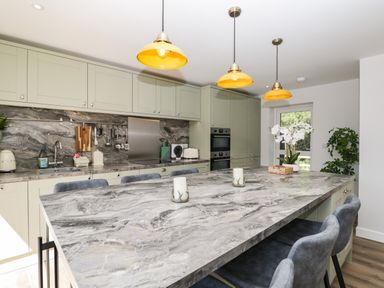 A kitchen with grey marble countertops green cabinets three hanging lights and bar stools at Stag Cottage in Lytchett Matravers