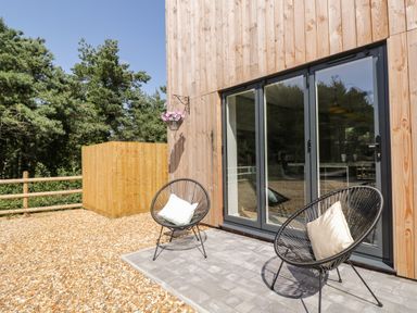 An outdoor patio with two black round chairs and cushions near glass doors at Stag Cottage in Lytchett Matravers