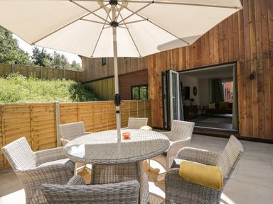 An outdoor patio with a round glass table surrounded by six wicker chairs and a large white umbrella at Stag Cottage in Lytchett Matravers
