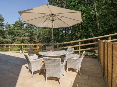 An outdoor patio with six wicker chairs around a round table and a large umbrella at Stag Cottage in Lytchett Matravers