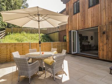 An outdoor patio with a round glass table and six wicker chairs under a large umbrella at Stag Cottage in Lytchett Matravers