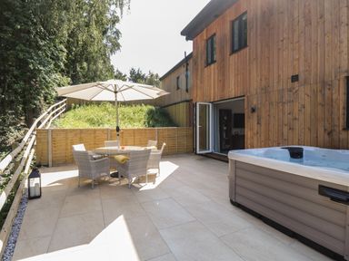 An outdoor patio with a round table and four chairs under an umbrella next to a hot tub at Stag Cottage in Lytchett Matravers