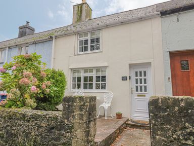 A front view of a cream colored house with white door and windows and a small patio with white chairs and a table at Ty Coed in Beaumaris