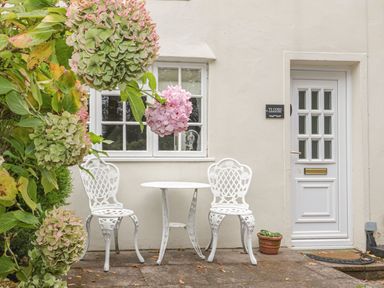 A small outdoor patio with two white metal chairs and a round table near a white door and window at Ty Coed in Beaumaris
