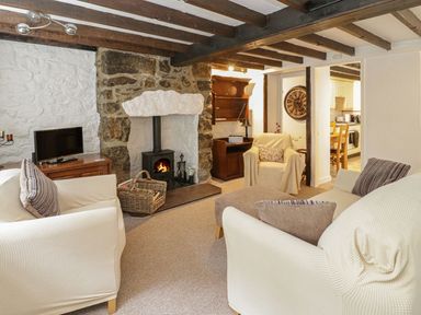 A living room with white sofas a stone fireplace a TV and a view into a kitchen at Ty Coed in Beaumaris
