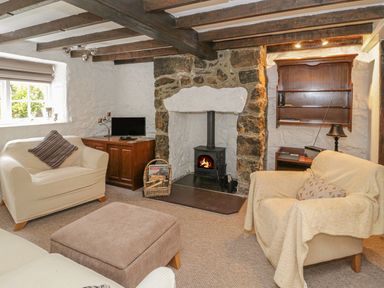 A living room with two armchairs a footstool a wood stove and wooden beams on the ceiling at Ty Coed in Beaumaris