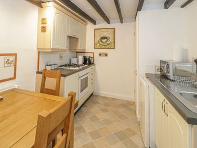A kitchen with wooden table and chairs gas stove microwave and sink at Ty Coed in Beaumaris