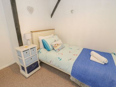 A single bed with patterned bedding and pillows next to a white chest of drawers with a lamp on top in a bedroom at Ty Coed in Beaumaris