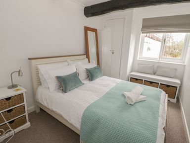 A bedroom with a bed two green cushions and rolled towels on the bed a bedside table with a lamp and a window seat with baskets at Ty Coed in Beaumaris