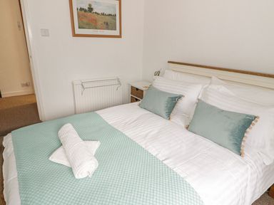 A bedroom with a double bed with cushions and folded towels on a blue bedspread at Ty Coed in Beaumaris