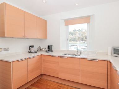 A kitchen with wooden cabinets a sink a microwave and appliances on the countertop with a window showing boats outside at 15 Dart Marina in Dartmouth
