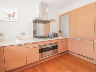 A kitchen with wooden cabinets a gas stove an oven a toaster and a knife block at 15 Dart Marina in Dartmouth