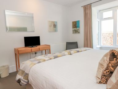 A bedroom with a bed facing a wooden desk with a television under a mirror at 15 Dart Marina in Dartmouth