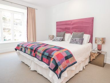 A bedroom with a double bed a pink headboard a multicolored blanket and two bedside tables with lamps at 15 Dart Marina in Dartmouth