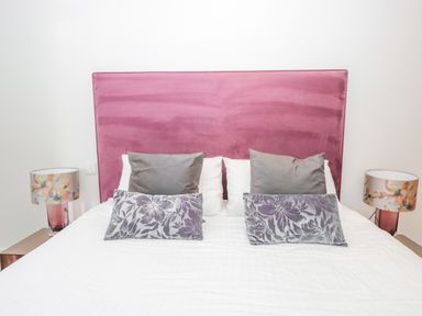 A bed with a pink headboard two gray pillows two patterned pillows and two floral lamps on bedside tables at 15 Dart Marina in Dartmouth