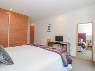 A bedroom with a bed a colorful blanket a large wooden wardrobe a desk with a computer and lamp a chair and a full-length mirror at 15 Dart Marina in Dartmouth