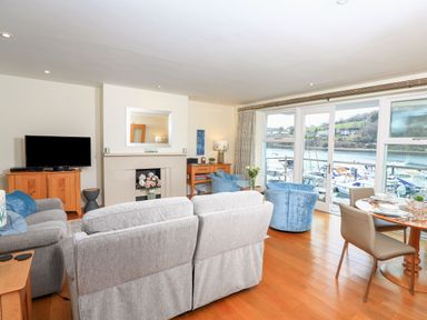A living room with sofas a TV and a dining table with a marina view at 15 Dart Marina in Dartmouth
