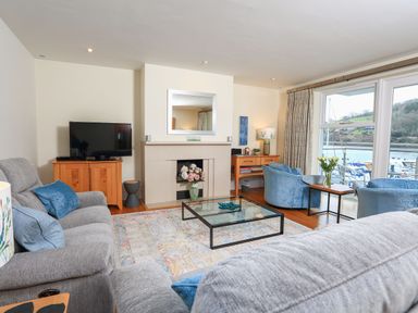 A living room with grey sofas a glass coffee table a fireplace TV and windows overlooking a marina at 15 Dart Marina in Dartmouth