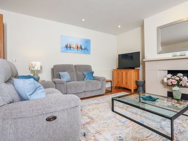 A living room with grey sofas a glass coffee table a TV on a wooden stand and a fireplace with flowers at 15 Dart Marina in Dartmouth