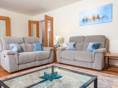 A living room with two gray sofas blue cushions a glass coffee table and a painting of sailboats at 15 Dart Marina in Dartmouth