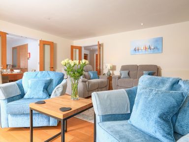 A living room with blue and beige armchairs a wooden table with flowers and glass doors opened at 15 Dart Marina Dartmouth